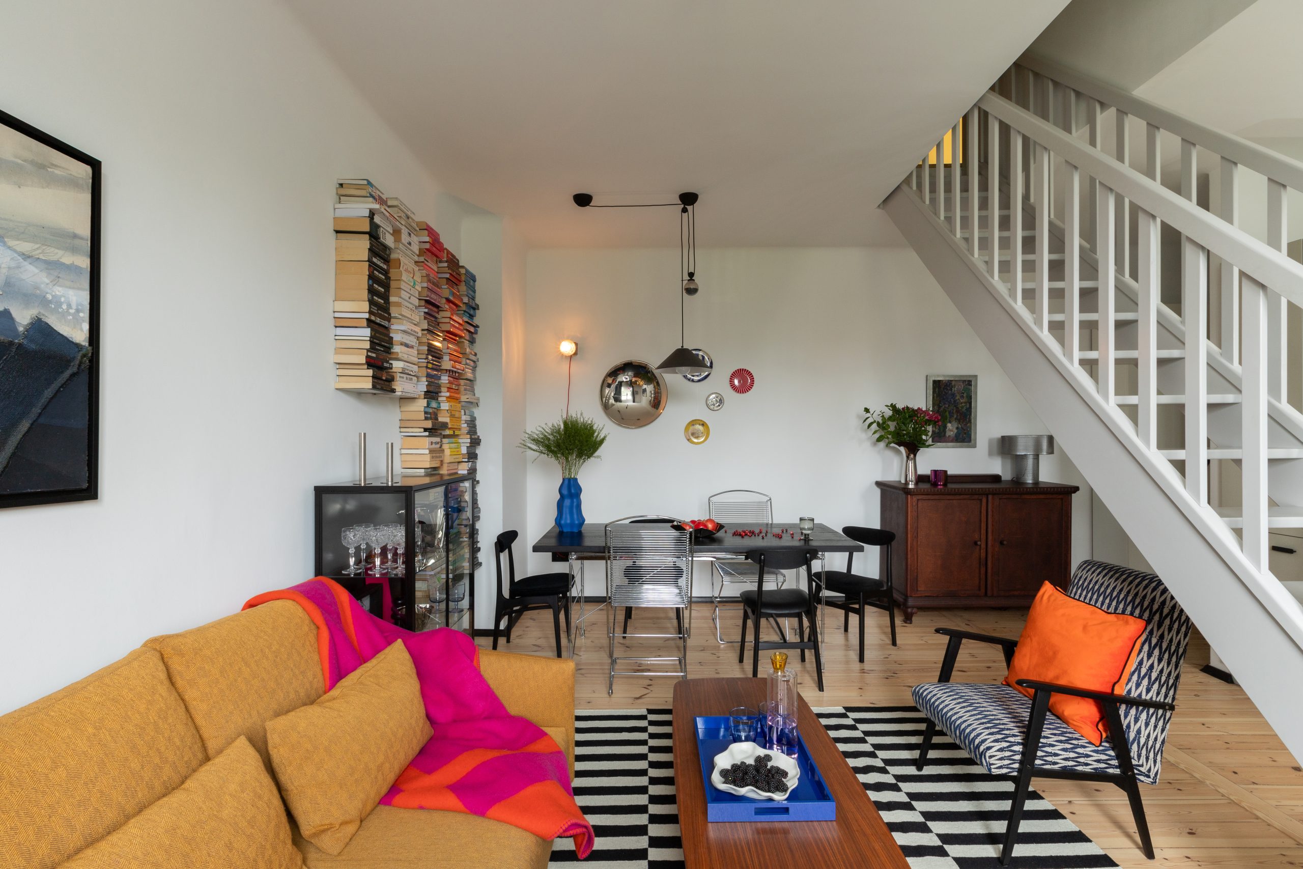 Eklektyczny salon w poznańskiej kamienicy zaprojektowany przez architekta wnętrz - autorska biblioteczka z kolorowym układem książek, designerski komplet wypoczynkowy w ciepłych barwach i kolekcja talerzy na ścianie